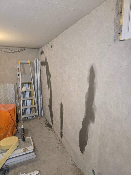 Källarvägg med reparerade sprickor, stege och byggmaterial; pågående renovering med fokus på väggarbete och elinstallation.