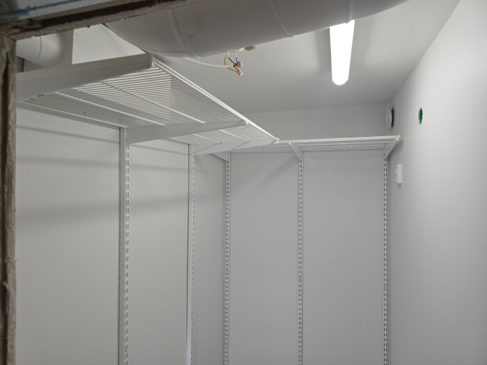 Klädkammare med nyligen monterade vita Elfa-hyllor och belysning i taket, synlig ventilationsrörledning.