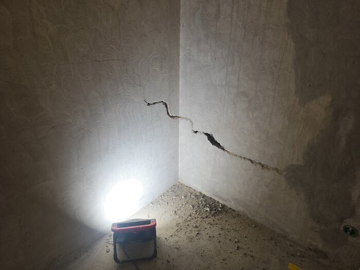 En vägg med en stor spricka och bygglampa som belyser området; materialet är delvis bortbrutet.