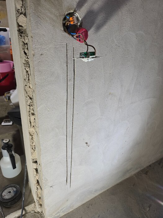 Installering av elektriskt uttag med synliga ledningar och skurna spår i väggen i en renoverad källare. Verktyg och utrustning syns i bakgrunden.