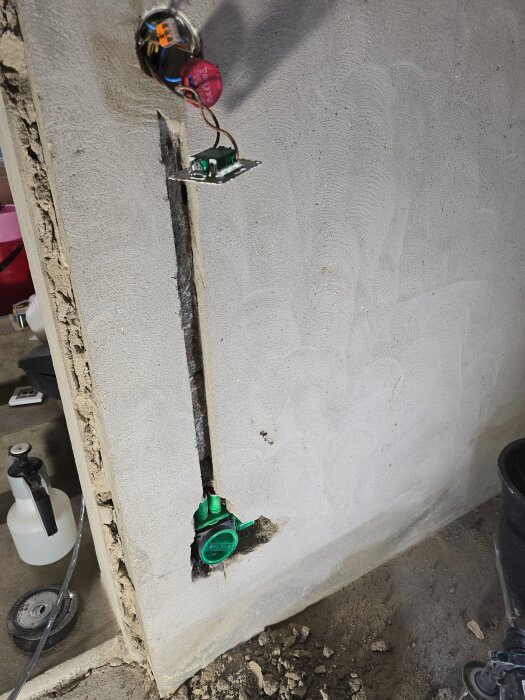 Installationsarbete av eluttag i en vägg med synliga kablar och ett delvis öppet uttag. Verktyg och byggmaterial syns runt omkring.