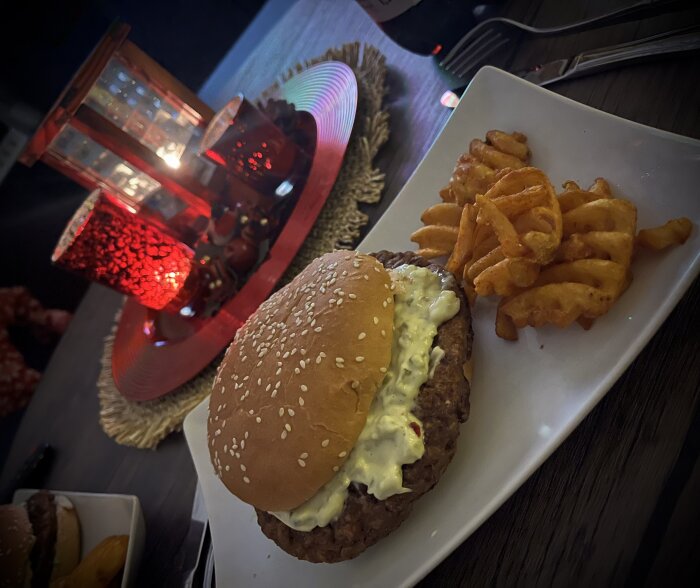 Hamburgare med jalapeñoost och gurksallad serverad med krusiga pommes på en tallrik, tända röda ljus bredvid.