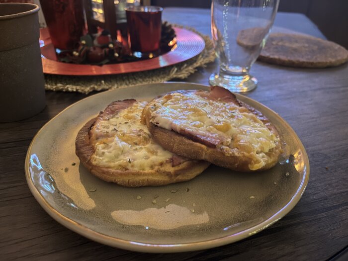 Två varma smörgåsar med julskinka och smält ost, beströdda med peppar och oregano, serverade på en tallrik på ett dukat bord.