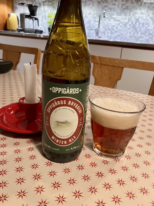 Flaska Oppigårds Winter Ale och ett glas öl på ett bord med julmönstrad duk, i bakgrunden syns köksinredning och en kaffebryggare.