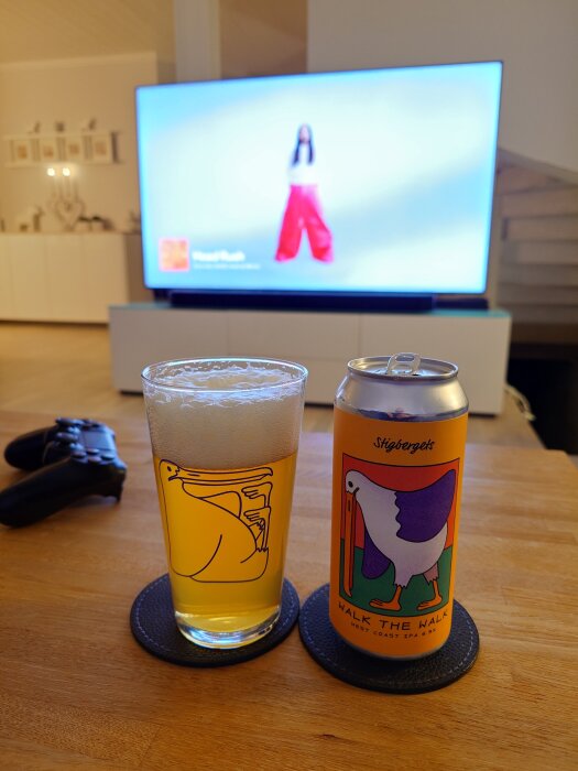 Ett glas öl bredvid en burk Stigbergets "Walk the Walk" IPA på ett bord, med en TV i bakgrunden.