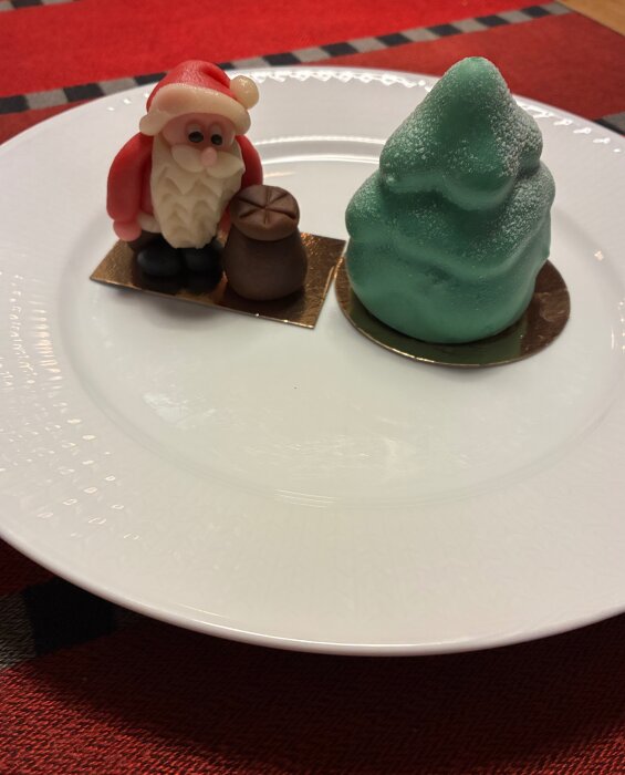 En tallrik med en julfigurin av en tomte och en grön julgran i sötmaterial på ett rött bord.