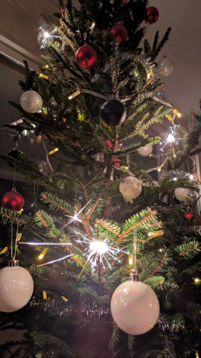 Julgran dekorerad med röda och vita julkulor, glittrande ljus och gnistrande stjärnor.