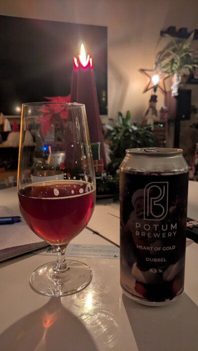 Ett glas rött öl bredvid en burk från Potum Brewery med texten "Heart of Gold Dubbel 6,5%" på ett bord med tända ljus i bakgrunden.