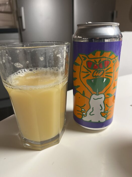 Ett glas med gul dryck bredvid en burk öl från Omnipollo, dekorerad med en tecknad tiger.