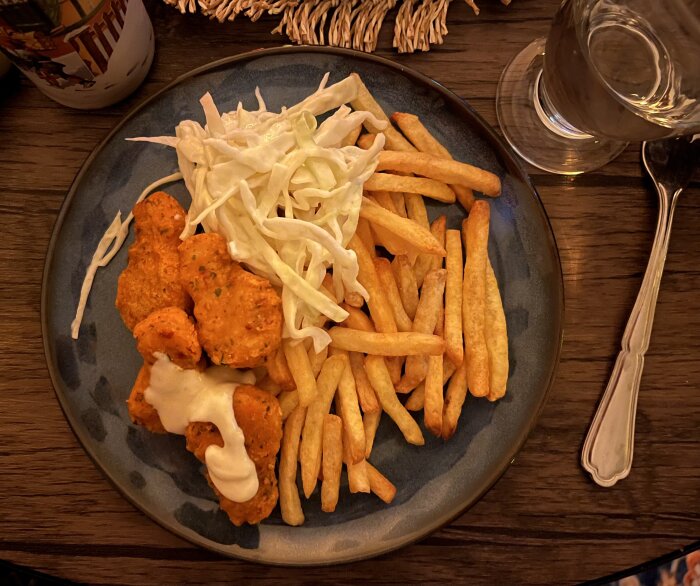 Tallrik med starka kycklingnuggets, pommes frites, coleslaw och sås.