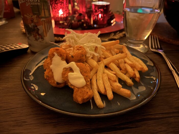 Kycklingnuggets med sås, pommes frites och coleslaw på en tallrik. Bakgrund i varma toner med tända ljus och ett glas vatten.