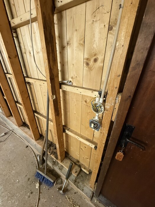 Oisolerad trävägg i garage under renovering, med synliga reglar, kablar och eluttag. Verktyg och borste på golvet.