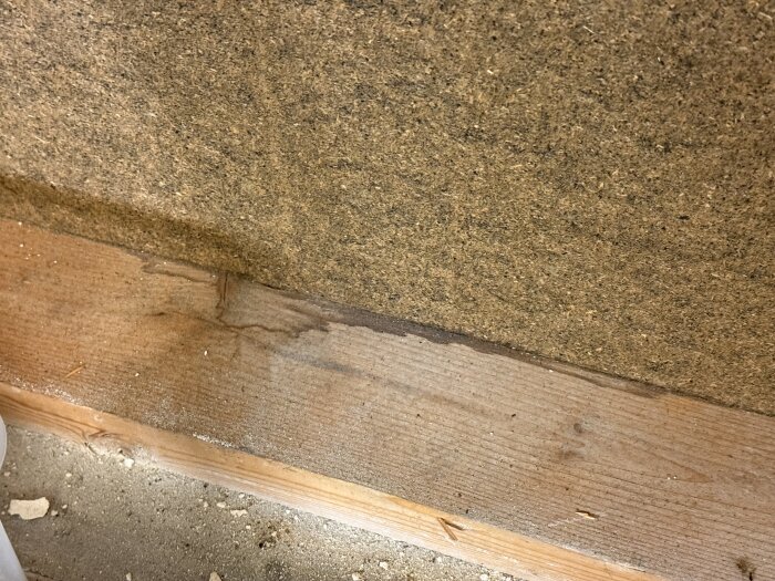 Fuktfläckar på träsyll och asfaboard i gammalt garage, potentiell orsak till dålig lukt och problem med ventilation och isolering.