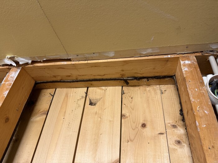 Träreglar och plywood i ett delvis rivet garage, synliga spår av fukt och skador, samt kablar i ett hörn.