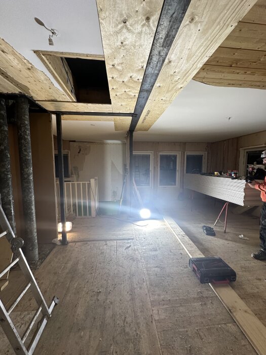 Renovering av innertak med en dold T-balk; byggarbetsplats med träpanel, stege och byggbelysning.