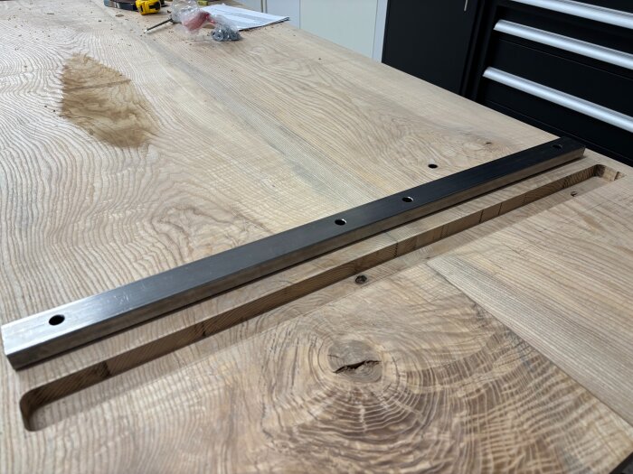 En fräst träyta med en metallstång placerad i ett spår, förberett för härdning med epoxy. I bakgrunden finns verktyg och tillbehör.