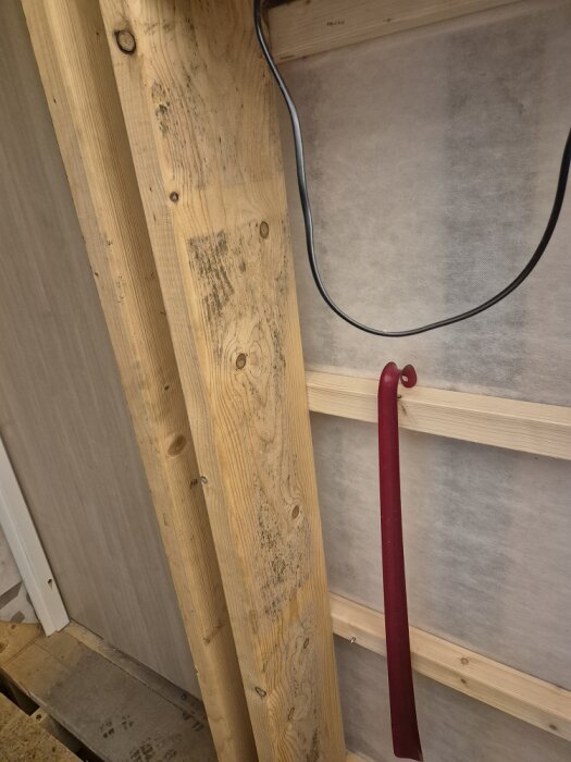 Träregel med mörka påväxter inomhus, ingen isolering synlig, och en röd föremål hänger på regeln.