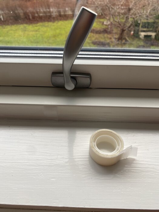 Fönsterhandtag och tejprulle på fönsterbräda, problem med att stänga vridfönster, försökt använda tejp utan framgång.