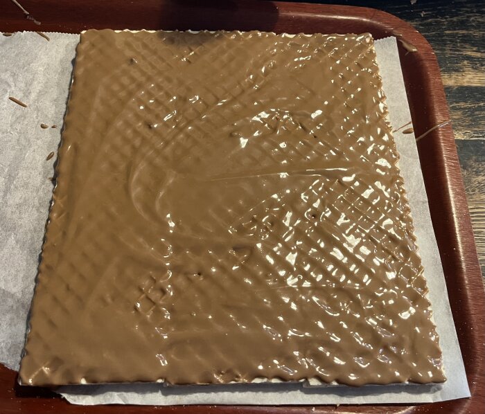 Hemmagjord kexchoklad med jordnötssmör och choklad på bakplåtspapper, redo att kylas och delas i bitar för fortsatt bearbetning.