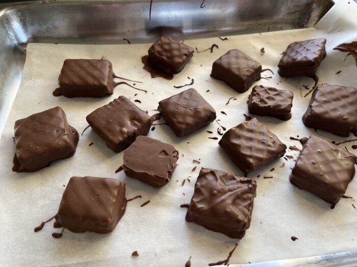 Hemmagjorda chokladdoppade kex, gjorda av smörgåsrån, jordnötssmör och choklad, ligger på ett bakplåtspapper för att stelna.