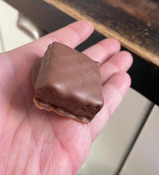 Hemgjord kexchoklad med jordnötssmör, chokladöverdrag och smörgåsrån, formad till en fyrkant och placerad på en hand.