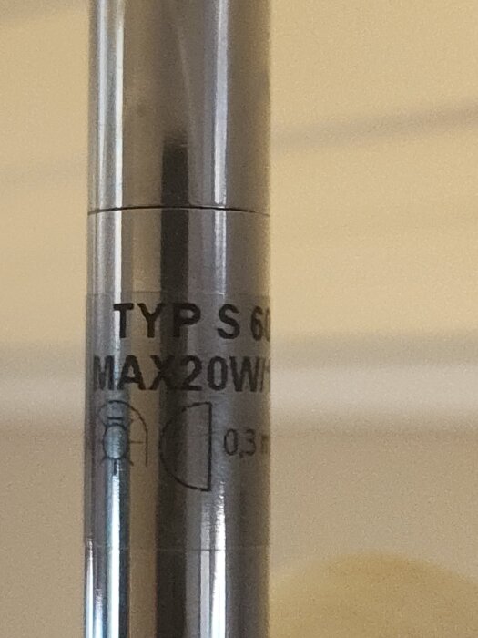 En närbild på en metallkomponent med texten: "Typ S 6012 Max 20W/12V" och en grafisk symbol.