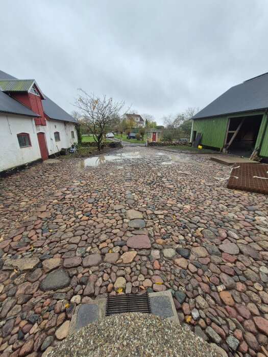 Stenlagd innergård rensad på ogräs, omgiven av byggnader. Synliga stenar i varierande storlekar och färger. Regniga förhållanden med vattenpölar.