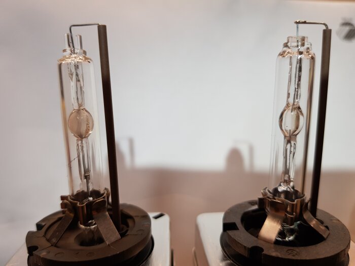 Två xenonlampor med stålfästen, placerade på en platt yta, med fokus på detaljrikedom i glaskroppen.