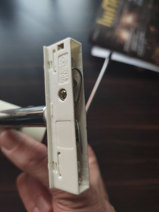 Närbild av en vit elektrisk dosa som hålls i handen, med synliga trådar och skruvanslutning.