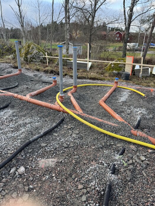Orange avloppsrör med rätt lutning installerade på grusmark, med gula och svarta kablar förberett inför isolering och kantelement.