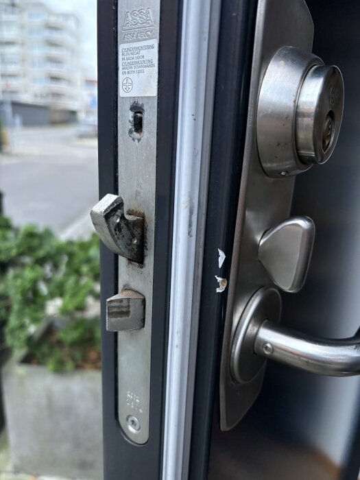 Närbild på ett dörrlås från märket ASSA, monterat på en dörrkarm. Låsets detaljer och dörrhandtaget är synliga i bilden.