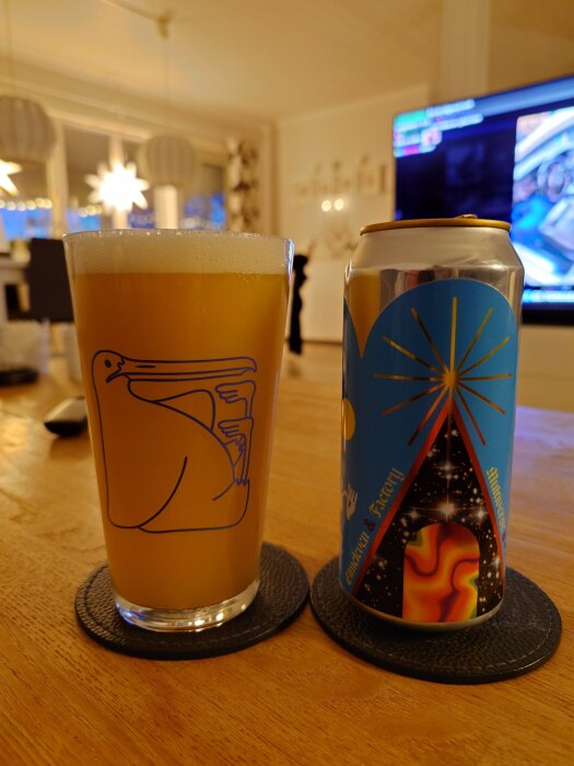 Ett glas öl med ett pelikanmotiv står bredvid en färgglad burk på ett bord, med en TV i bakgrunden i ett upplyst rum.