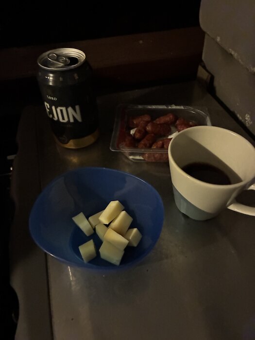 Ölburk med texten "Lejon", skål med ostbitar, förpackning med charkuterier och kopp på bordet.