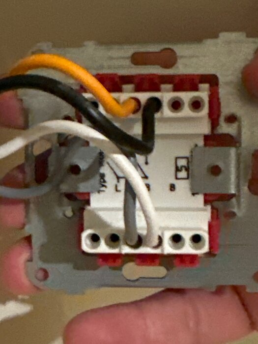 En elektrisk brytare med dubbelknappar, ansluten med flera färgade kablar, monterad på en väggplatta.