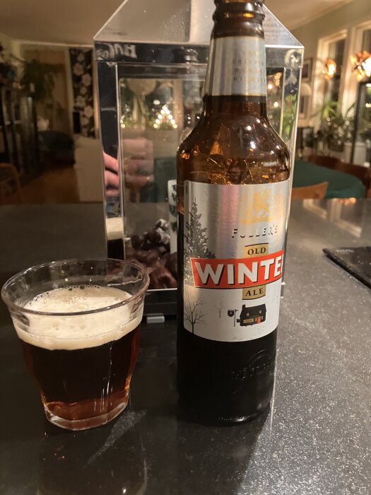 Flaska med Fuller's Old Winter Ale och ett glas med öl på ett bord i ett hemtrevligt interiör.