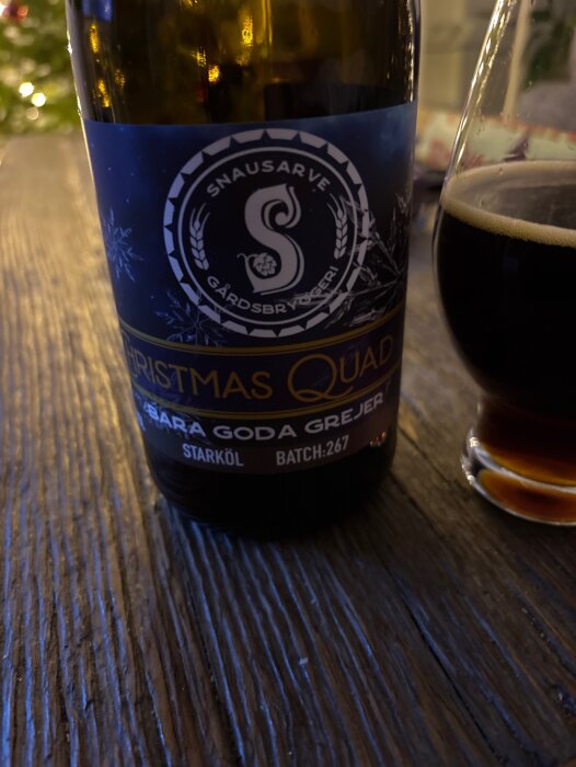 Flaska med julöl från Snausarve Gårdsbryggeri, etiketten visar "Christmas Quad" och ett glas med mörkt öl.
