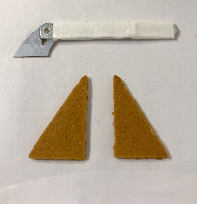 Två triangulära pepparkaksbitar och ett verktyg med vitt handtag, förberett för att bygga pepparkakshus inspirerat av Kiruna kyrka.