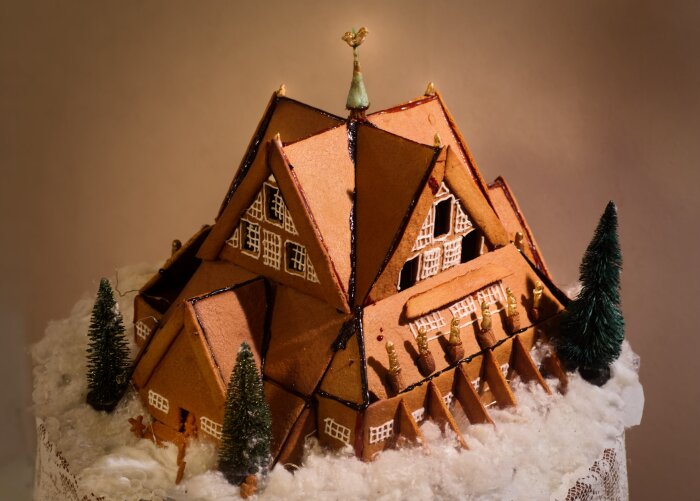 Pepparkaksmodell av Kiruna kyrka med detaljer i marsipan och smält socker, omgiven av konstsnö och små granar, avbildad med ytterbelysning.
