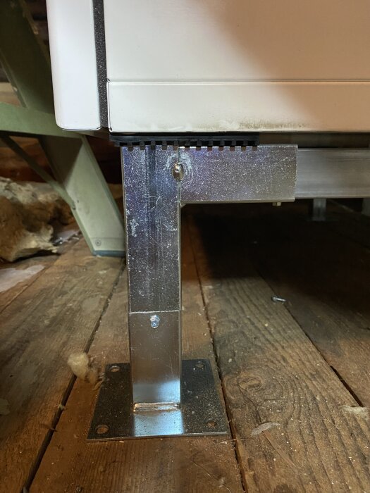 Metallstöd med gummimatta under ett vitvaruskåp på träplankgolv.