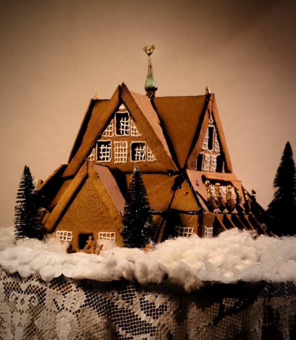 Pepparkaksmodell av Kiruna kyrka med detaljer av marsipan och spaghetti, placerad på en snöliknande duk, med träd av pepparkaksträd.