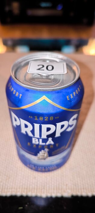 Blå burk med Pripps Blå Export öl med en etikett som har nummer 20 på toppen, placerad på ett bord.