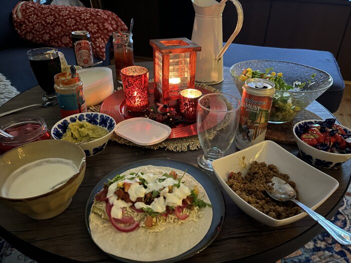 Tacobord med tortilla, såser, grönsaker och köttfärs. Julmust och godisskål syns bredvid tända ljus på bordet.