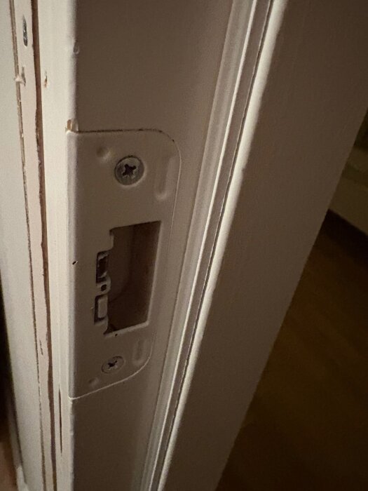 Närbild på en dörrkarm med en urholkning för lås, visar detaljer av karmens kanter och skruvar.