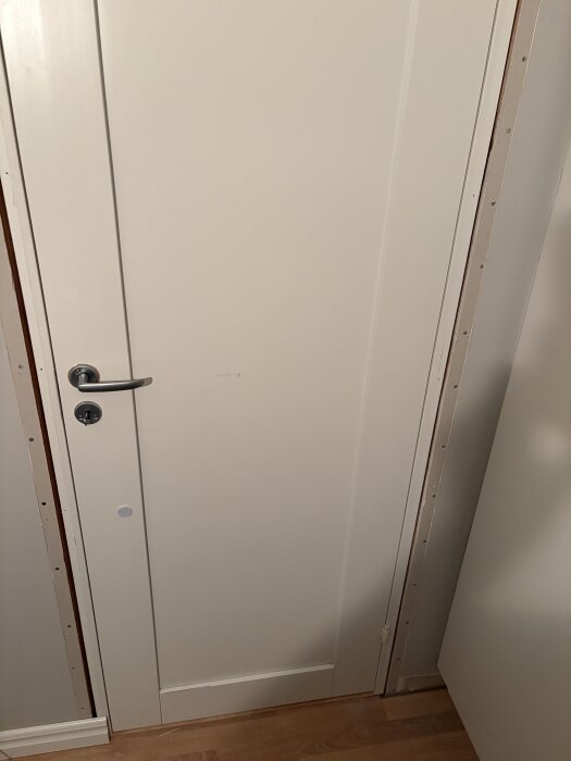 Vit innerdörr med karm, omgiven av ofärdiga ytor. Dörromfattningen är synlig där drevning planeras.
