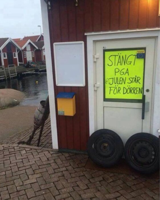 Röd byggnad vid kaj med ett gult papper på dörren med texten "Stängt pga julen står för dörren", däck lutade mot väggen.