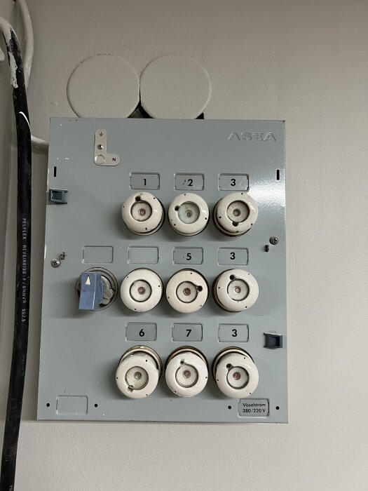Gammalt elskåp med flera porslinssäkringar och spakar, märkta med nummer och anteckningen "Växelström 380/220 V".