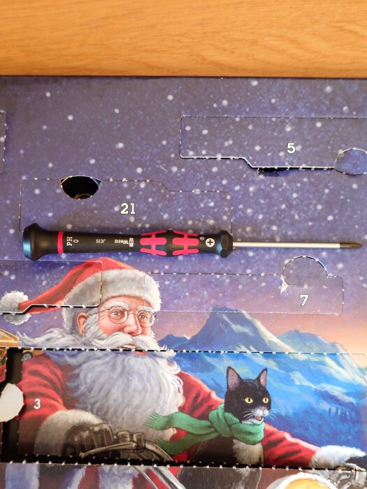 Julkalender med skruvmejsel framför bild på jultomten och en katt i snölandskap.