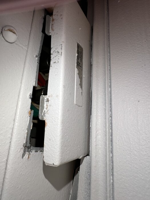 Väggmonterad, delvis öppen elbox med trasig målning och synliga ledningar.