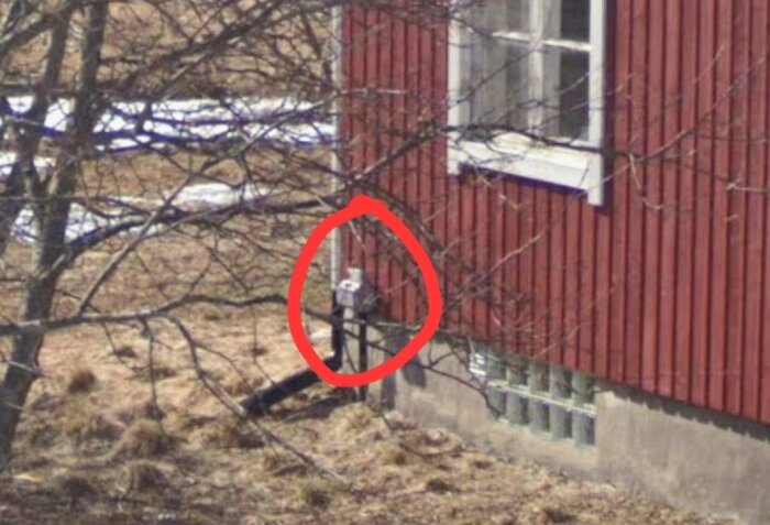 Liten låda med huvudsäkringar på utsidan av ett rött hus markerad med röd cirkel.
