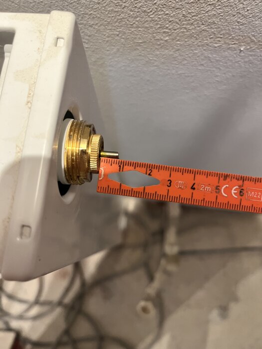 Ventil med röd måttstock som mäter längden på en kortare termostatventil på ett element.
